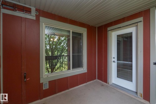 Covered outdoor patio area featuring a concrete floor, red siding, and white trim - 208 3719 Whitelaw Lane, Edmonton, AB 