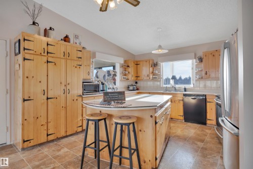 Kitchen with a kitchen breakfast bar, light brown cabinetry, light countertops, stainless steel appliances, and lofted ceiling - A49375 Rr 243, Rural Leduc County, AB 