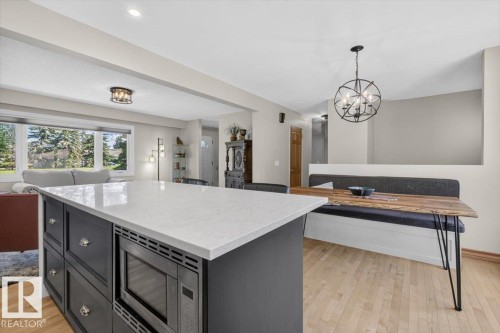 Kitchen island with a light-toned countertop and built-in microwave, dark cabinetry with decorative hardware, and light wood-finish flooring - 10736 48 Street, Edmonton, AB 