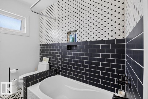 Bathroom featuring a white soaking tub with matte black fixtures, black subway tile, and white hexagonal tile with black accents - 10736 48 Street, Edmonton, AB 