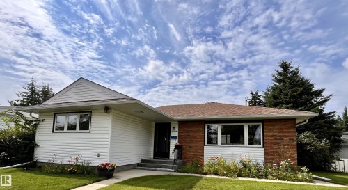Exterior featuring white siding, brick accents, a brown shingle roof, and a mature tree - 10736 48 Street Nw, Edmonton, AB - Outdoor