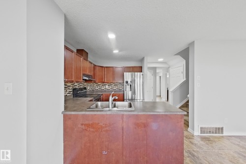 Kitchen featuring wood cabinetry, stainless steel sink with gooseneck faucet, dark countertops, and mosaic tile backsplash - 1806 28 Street Nw, Edmonton, AB 