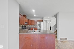 Kitchen featuring wood cabinetry, stainless steel sink with gooseneck faucet, dark countertops, and mosaic tile backsplash - 