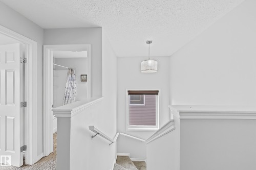 Upper-level landing featuring a contemporary drum pendant light, a window with a cellular shade, and a white handrail leading to the lower level - 1806 28 Street Nw, Edmonton, AB 