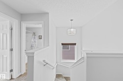 Upper-level landing featuring a contemporary drum pendant light, a window with a cellular shade, and a white handrail leading to the lower level - 