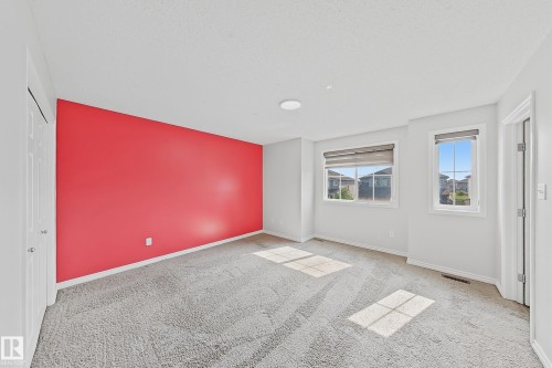 Spacious room featuring a vibrant accent wall, two large windows with horizontal blinds, and neutral grey carpeting - 1806 28 Street Nw, Edmonton, AB 