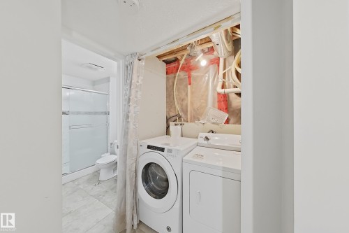 Laundry area with a side-by-side washer and dryer, featuring an adjacent bathroom with a glass-enclosed shower, toilet, and tiled flooring - 1806 28 Street Nw, Edmonton, AB 