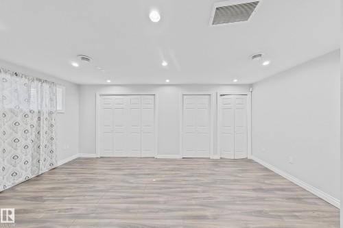 Spacious room featuring wood-finish flooring, white baseboards, and bright recessed lighting - 1806 28 Street Nw, Edmonton, AB 