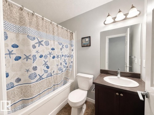 Bathroom featuring a white bathtub, a dark wood-finish vanity with an integrated sink, a rectangular mirror, and a three-light vanity fixture - 1806 28 Street Nw, Edmonton, AB 