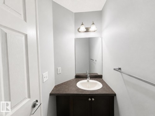 Powder room featuring a single-basin sink, dark wood-finish vanity, and wall-mounted mirror - 1806 28 Street Nw, Edmonton, AB 