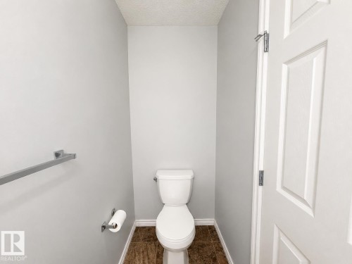 Compact water closet featuring a two-piece toilet, light gray walls, textured ceiling, brown-toned floor tiles, and white trim - 1806 28 Street Nw, Edmonton, AB 