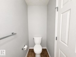 Compact water closet featuring a two-piece toilet, light gray walls, textured ceiling, brown-toned floor tiles, and white trim - 