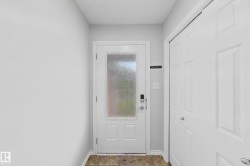 Entryway featuring a white door with frosted glass panel and smart lock, complemented by light gray walls and brown tiled flooring - 