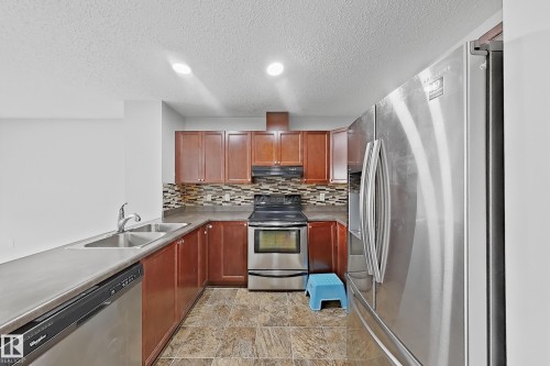 Kitchen featuring stainless steel appliances, wood cabinetry, a mosaic tile backsplash, and durable countertop surfaces - 1806 28 Street Nw, Edmonton, AB 