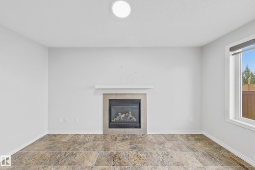 Living area featuring a gas fireplace with a tiled surround and mantle, large window with a roller shade, and wood-finish flooring - 1806 28 Street Nw, Edmonton, AB 