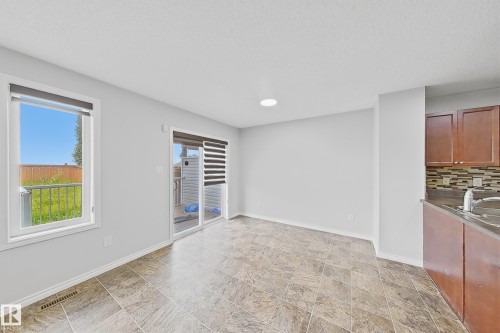 Spacious room featuring neutral paint, patterned tile flooring, a large window, and a sliding glass door providing exterior access - 1806 28 Street Nw, Edmonton, AB 