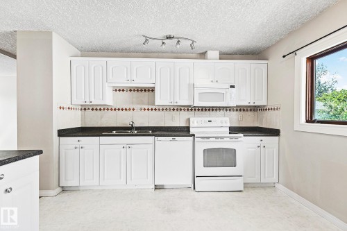 Kitchen featuring white cabinetry, dark countertops, a tiled backsplash with decorative border, white appliances, and a track lighting fixture - 17059 98 Street, Edmonton, AB - Indoor Photo Showing Kitchen With Double Sink
