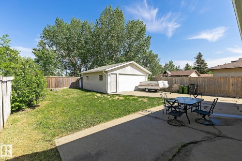 Expansive backyard featuring a detached garage with an overhead door, a concrete patio area, a grassy lawn, and perimeter wood fencing - 17059 98 Street, Edmonton, AB - Outdoor