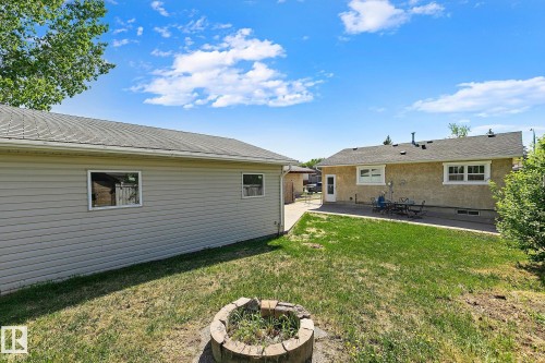 Expansive backyard featuring a stone-lined fire pit, a detached garage with horizontal siding, and a concrete patio - 17059 98 Street, Edmonton, AB - Outdoor