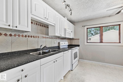 Kitchen featuring white cabinetry with brushed nickel hardware, speckled dark countertops, a double basin stainless steel sink, and a tile backsplash with decorative diamond accents - 17059 98 Street, Edmonton, AB - Indoor Photo Showing Kitchen With Double Sink