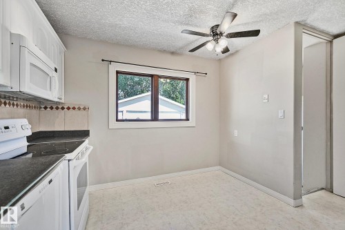 Kitchen dining area featuring white cabinetry, dark countertops, a built-in microwave, tile backsplash, and a ceiling fan with light fixture - 17059 98 Street, Edmonton, AB - Indoor Photo Showing Kitchen