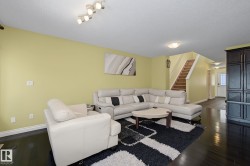 Spacious living area featuring dark wood-finish flooring, light-toned wall paint, and a visible staircase with wood treads - 