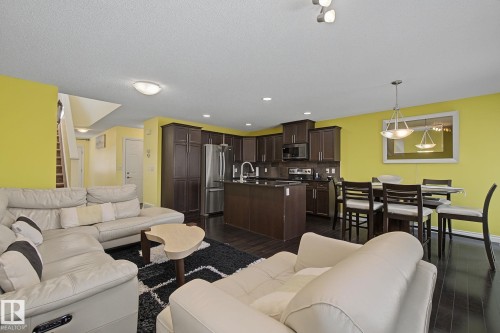 Open-concept living area with dark wood-finish flooring, a kitchen featuring dark cabinetry and stainless steel appliances, and a dining space illuminated by a pendant light fixture - 5205 168 Avenue, Edmonton, AB 
