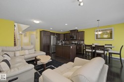 Open-concept living area with dark wood-finish flooring, a kitchen featuring dark cabinetry and stainless steel appliances, and a dining space illuminated by a pendant light fixture - 