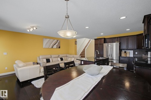 Open-concept living space featuring wood-finish flooring, a kitchen island with dark countertops, stainless steel appliances, and a staircase with a wood handrail - 5205 168 Avenue, Edmonton, AB 