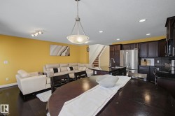 Open-concept living space featuring wood-finish flooring, a kitchen island with dark countertops, stainless steel appliances, and a staircase with a wood handrail - 