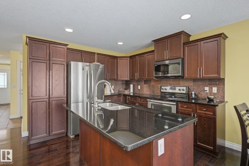 Kitchen featuring a central island with a sink, dark wood-finish cabinetry, stainless steel appliances, dark countertops, and recessed lighting - 5205 168 Avenue, Edmonton, AB 