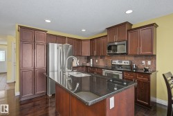 Kitchen featuring a central island with a sink, dark wood-finish cabinetry, stainless steel appliances, dark countertops, and recessed lighting - 