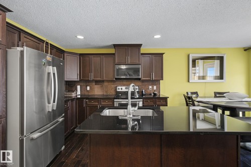 Kitchen featuring dark wood-finish cabinetry, stainless steel appliances, dark countertops, and a central island with an undermount sink - 5205 168 Avenue, Edmonton, AB 
