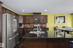 Kitchen featuring dark wood-finish cabinetry, stainless steel appliances, dark countertops, and a central island with an undermount sink - 