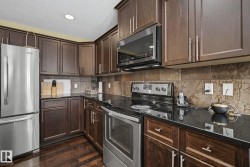 Kitchen featuring dark wood cabinetry, black countertops, stainless steel appliances, a tile backsplash, and wood-finish flooring - 