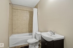 Full bathroom featuring a white bathtub, beige tiled shower surround, dark wood-finish vanity with an integrated white sink, and chrome fixtures - 