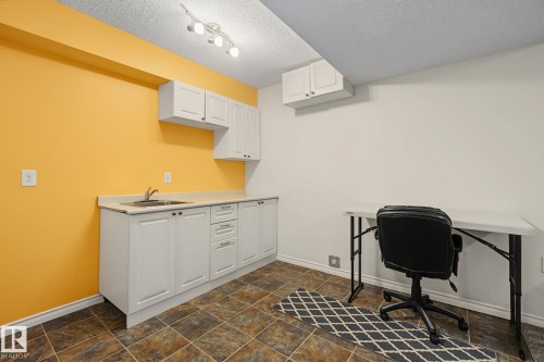 Utility area featuring a sink with a stainless steel faucet, white cabinetry, light-toned countertops, and textured tile flooring - 5205 168 Avenue, Edmonton, AB 