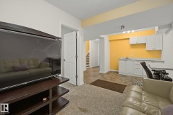 Lower level recreation area featuring carpeted flooring, a separate wet bar with white cabinetry and a sink, tiled flooring in the wet bar area, and an open doorway leading to a staircase - 