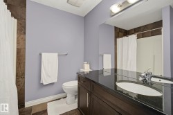 Bathroom featuring a dark wood-finish vanity with an integrated oval sink, a wall-mounted mirror, overhead vanity lighting, and a shower with brown tile surround - 