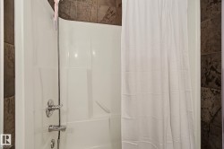 White fiberglass tub and shower combination with chrome fixtures, surrounded by large format wall tile - 
