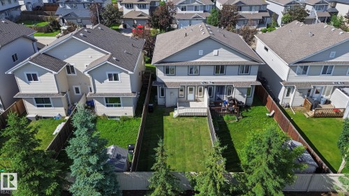 Rear exterior featuring a spacious fenced yard, wooden deck, mature evergreen trees, and light-colored siding - 5205 168 Avenue, Edmonton, AB 