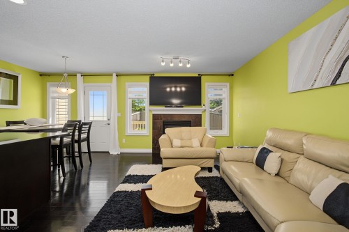 Open-concept living area featuring rich dark wood-finish flooring, a built-in fireplace with a stone surround, and an integrated media wall - 5205 168 Avenue, Edmonton, AB 