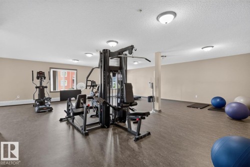 Spacious fitness room featuring durable flooring, multiple exercise machines, and flush-mount ceiling lighting - 103 2203 44 Avenue, Edmonton, AB 