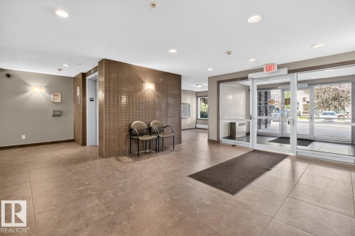 Spacious lobby featuring large format tile flooring, a tiled accent wall, recessed lighting, and a glass entrance system - 103 2203 44 Avenue, Edmonton, AB 