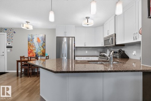 Kitchen featuring a granite-look island, white cabinetry, stainless steel appliances, and wood-finish flooring - 103 2203 44 Avenue, Edmonton, AB 