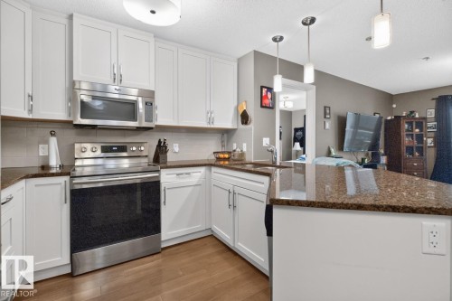 Kitchen featuring white cabinetry with brushed nickel hardware, a stainless steel appliance suite, speckled stone countertops, a light-toned tile backsplash, and wood-finish flooring - 103 2203 44 Avenue, Edmonton, AB 