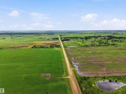 Expansive rural landscape featuring a long unpaved road, cultivated fields, a natural pond, and distant tree lines - 55111 Range Road 230, Rural Sturgeon County, AB 