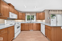Bright kitchen featuring wood-finish cabinetry, white appliances, and light countertops - 