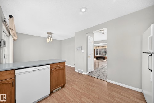 Kitchen area featuring wood-finish flooring, white built-in dishwasher, light gray countertops, and wood cabinetry - 51 9630 176 Street, Edmonton, AB 