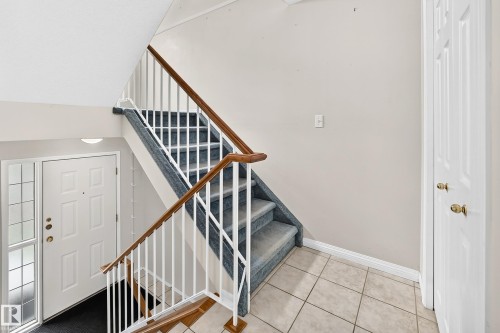 Foyer featuring a white paneled entry door with sidelight, tile flooring, and carpeted stairs with white balusters and wood handrails - 51 9630 176 Street, Edmonton, AB 